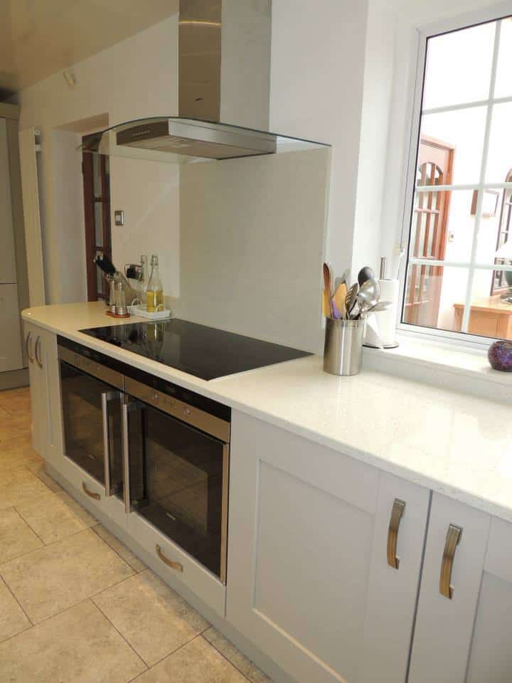 TWO OVENS SIDE by side of beige cabinets , an induction hob is above with a stainless steel extractor