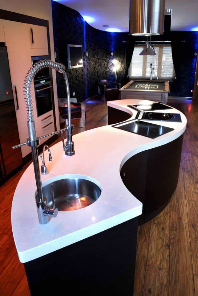 An s shaped fitted kitchen island with a sink and tap inset along with three hobs alongside