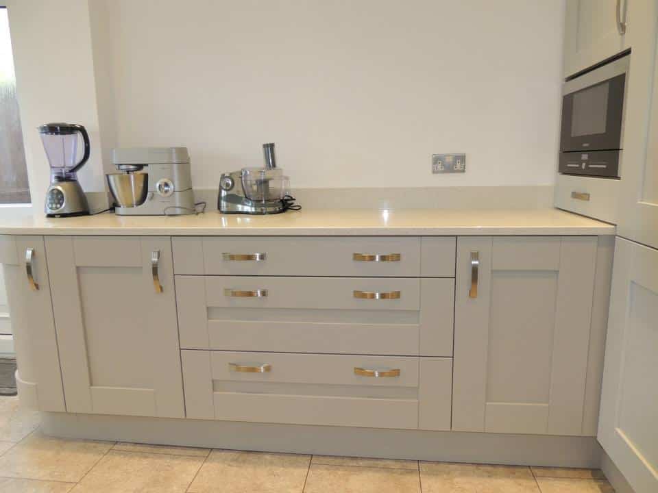a wide set of drawers in beige either side of base cabinets also in beige , a cream light quartz top is on top