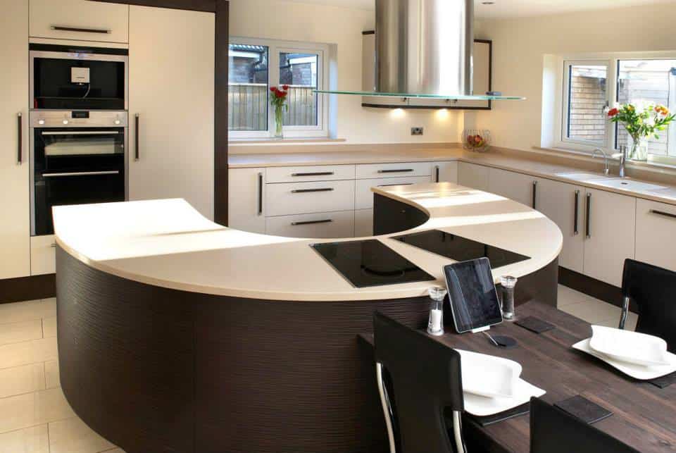 fitted kitchen in Teesside with a timber table fixed to a u shape island with a hob , to th erear tall cabinets with fridge an dfreezer hisdden an dovens at a height , wenge and porcelain doors all wrapped in wenge frame