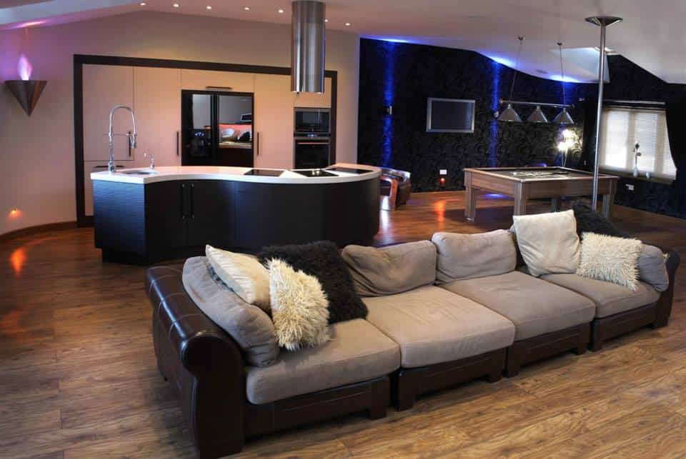 a view of a fitted kitchen form the lounge showing an s shaped island with a stainless steel extractor and open plan