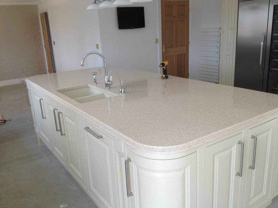 An Astor kitchen with an island and sink , having curved cabinets on each side light coloured doors and light worksurface reflect the light back into the room,