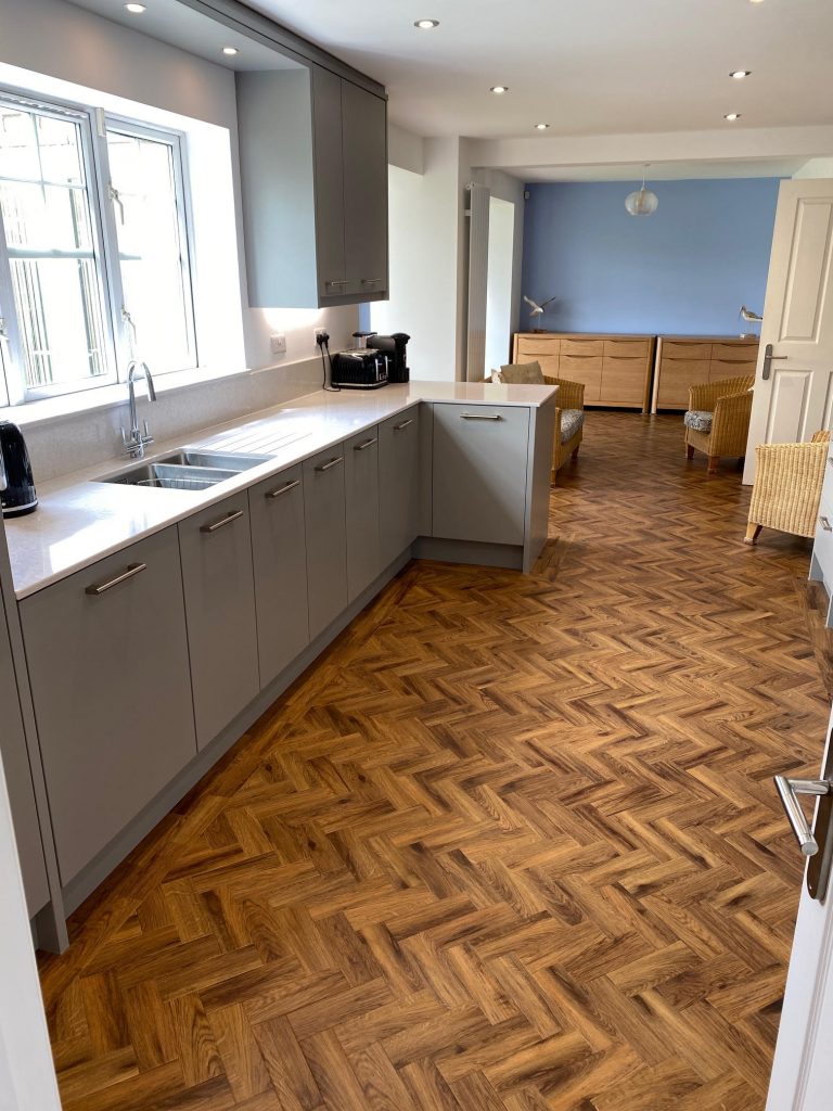 Fitted kitchen in Teesside by Court Homemakers showing a sink under a wwindow and a long run of base cabinets until a corner cabinet is pulled back into the room creating an l shape