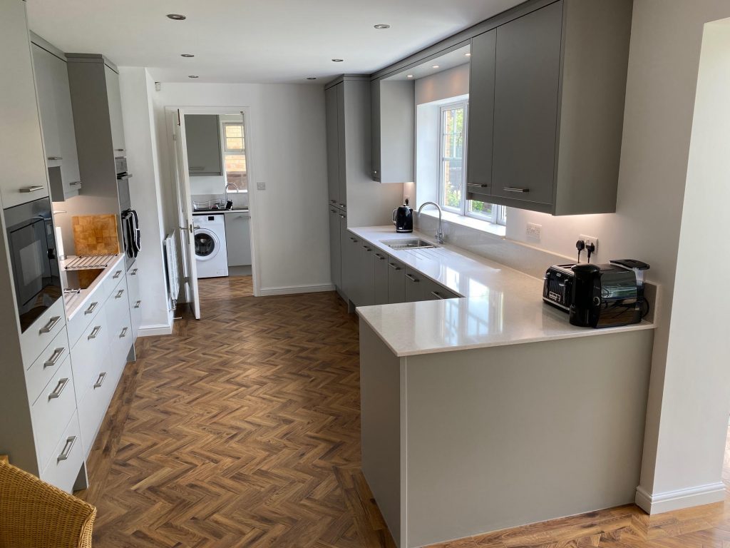 Fitted kitchen in Teesside by Court Homemakers where a galley kitchen is shown with a long bank of base cabinets and sink are beneath a window, two wall cabinets are either side of the window