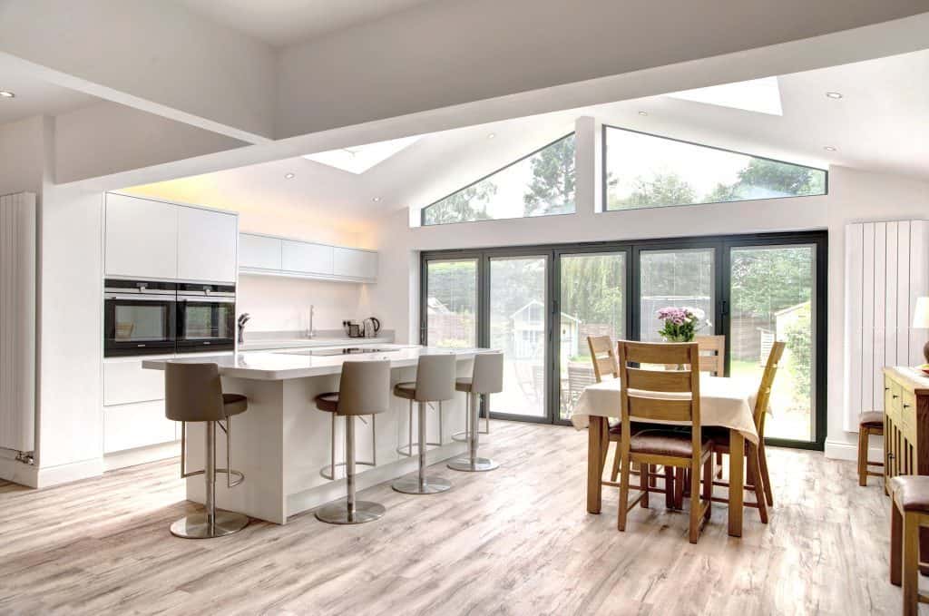 Fitted Kitchen in Middlesbrough With Breakfast Bar seating at an island and ovens in tall units looking out through large patio doors to a garden