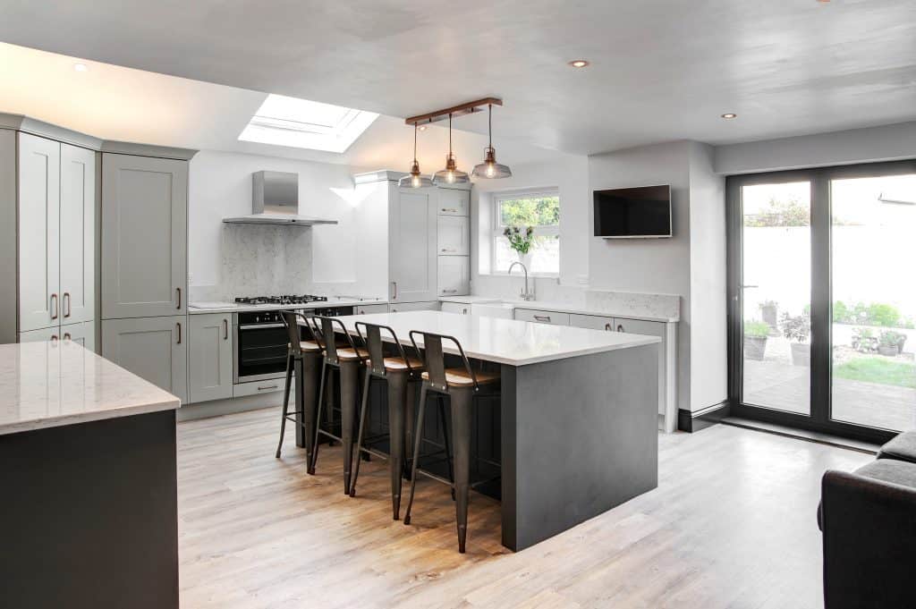 seating area at an grey island with quartz top , in the background two built under ovens and a hob can be seen, Shaker Kitchen,