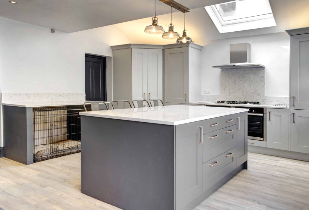 large grey island with light quartz top .wide drawers in centre of two single base cabinets, mood lighting above with three pendants