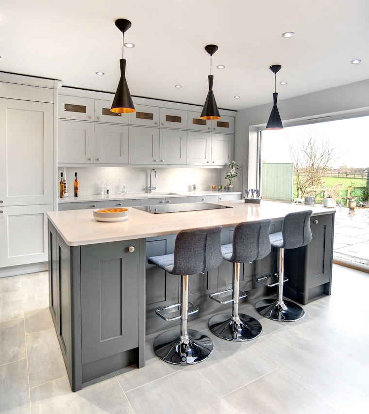 fitted KITCHEN WITH AN ISLAND WITH SEATING FOR THREE AND A HOB IN THE CENTRE , AT THE BACK SOME GLASS CABINETS ON THE WALL ABOVE SOME GREY CABINETS WITH LIGHT QUARTZ SURFACES